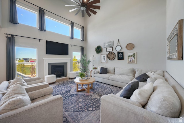 living area with a ceiling fan, a high ceiling, and a glass covered fireplace