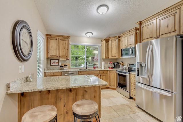 1155 S 2880 E, Spanish Fork, UT 84660 - kitchen featuring a breakfast bar area, a textured ceiling, appliances with stainless steel finishes, a sink, and a peninsula