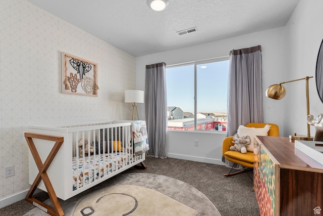carpeted bedroom with visible vents, baseboards, a crib, and wallpapered walls