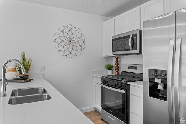 kitchen with appliances with stainless steel finishes, a sink, light countertops, light wood finished floors, and white cabinetry