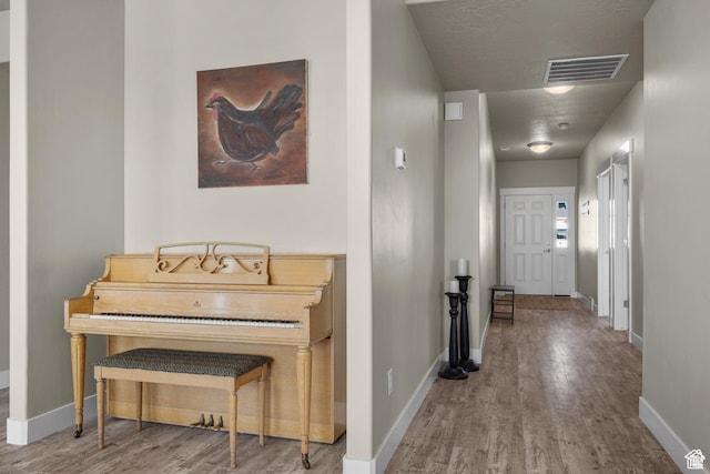 hall featuring baseboards, wood finished floors, and visible vents