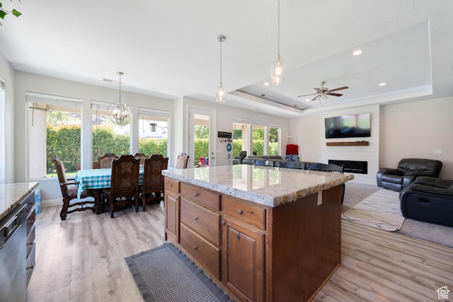 kitchen with light stone countertops, light wood-style floors, a raised ceiling, a large fireplace, and ceiling fan with notable chandelier