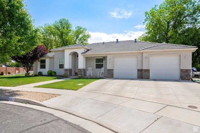 single story home with a tiled roof, a front yard, a garage, concrete driveway, and stone siding