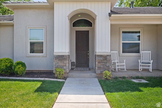 entrance to property with stucco siding, a yard, and stone siding