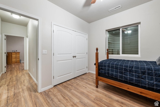 bedroom with ceiling fan, visible vents, light wood-type flooring, baseboards, and a closet