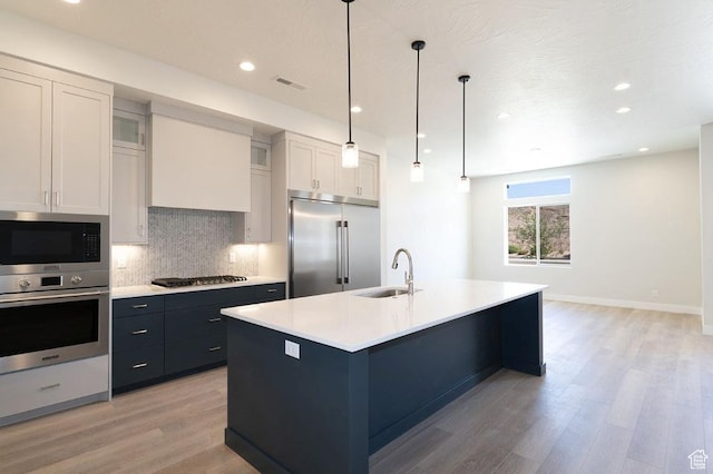kitchen featuring backsplash, visible vents, a sink, light wood finished floors, and built in appliances