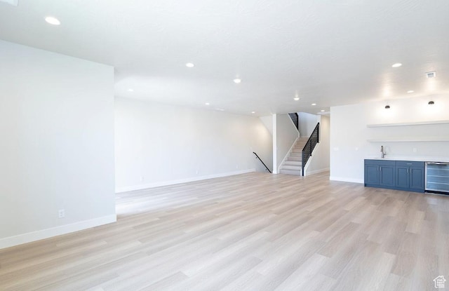 unfurnished living room with a sink, light wood-style floors, beverage cooler, indoor wet bar, and stairs