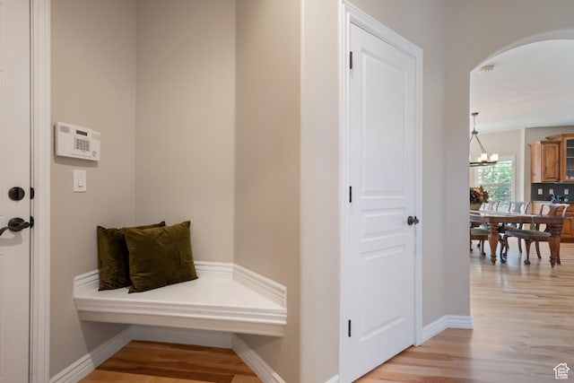 mudroom featuring arched walkways, light wood-style floors, a chandelier, and baseboards