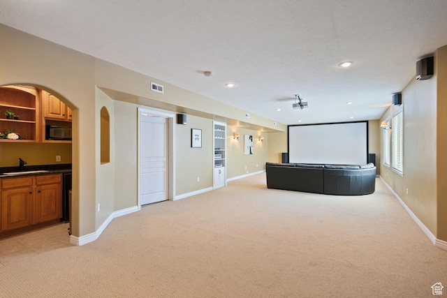 home theater room with baseboards, a sink, visible vents, and light colored carpet