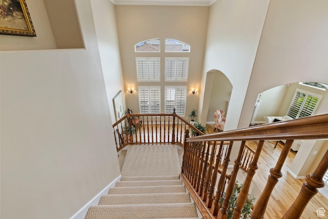 stairs featuring crown molding, baseboards, a towering ceiling, and arched walkways