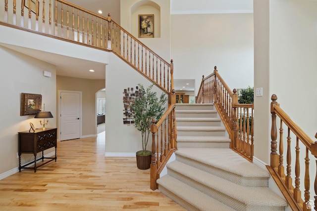 stairway featuring wood finished floors, a high ceiling, baseboards, arched walkways, and recessed lighting