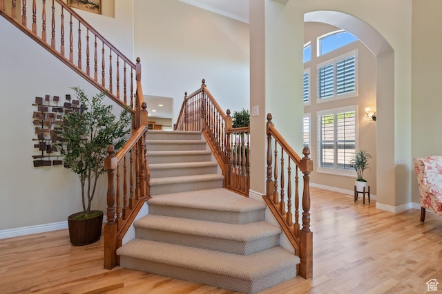 stairway with wood finished floors, baseboards, and a high ceiling