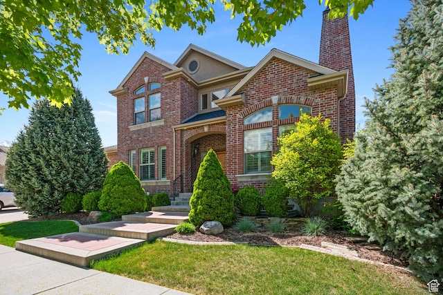 traditional home featuring a chimney, a front yard, and brick siding