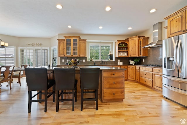 kitchen with brown cabinetry, stainless steel appliances, a breakfast bar area, wall chimney exhaust hood, and a center island
