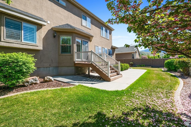 rear view of property with fence, a patio, stucco siding, and a lawn