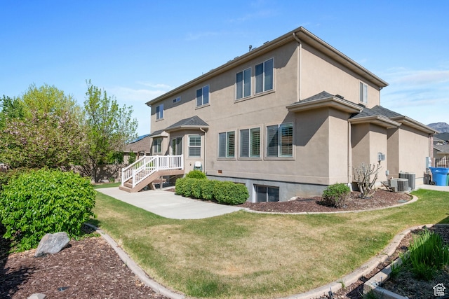 rear view of house with a yard, stucco siding, and central AC