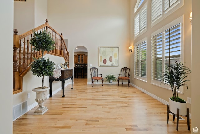 sitting room featuring baseboards, visible vents, arched walkways, light wood-style floors, and a high ceiling