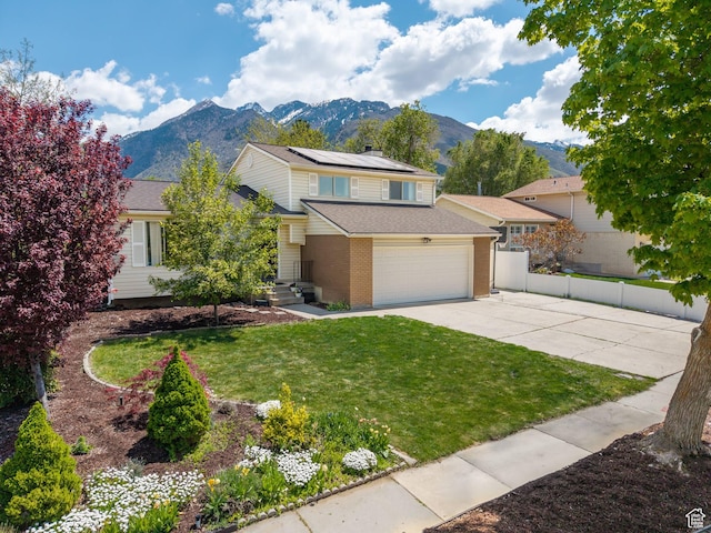 view of front of house featuring a front yard, fence, roof mounted solar panels, a mountain view, and concrete driveway