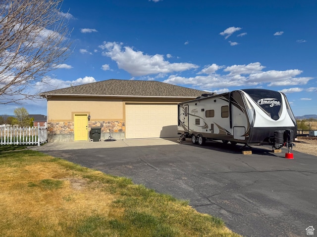 view of side of home with fence, stone siding, stucco siding, an attached garage, and driveway