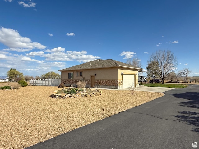 view of side of property with a garage, fence, concrete driveway, stone siding, and stucco siding