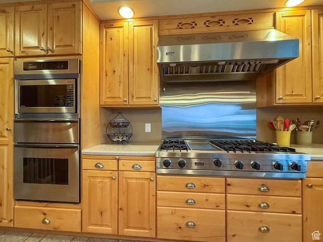kitchen featuring light countertops, range hood, appliances with stainless steel finishes, and a warming drawer