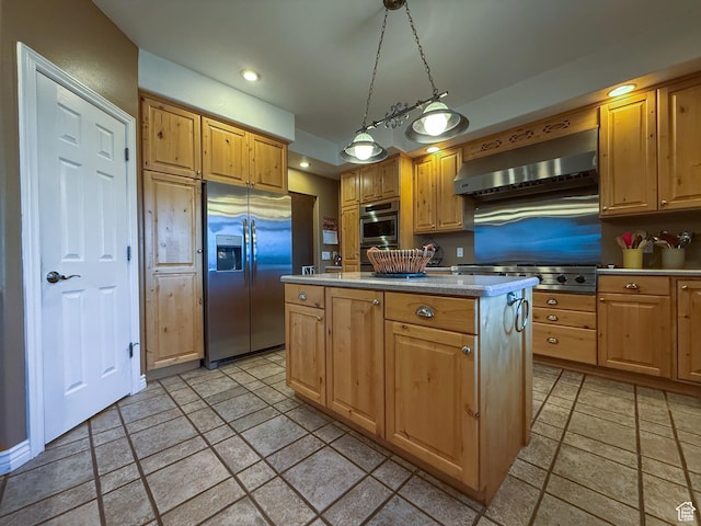 kitchen with appliances with stainless steel finishes, light countertops, wall chimney exhaust hood, stone tile floors, and a kitchen island
