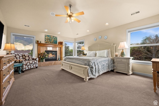 carpeted bedroom with visible vents, a tiled fireplace, and multiple windows