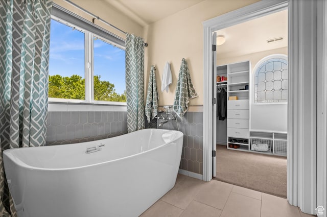bathroom with wainscoting, tile walls, a walk in closet, tile patterned floors, and a soaking tub