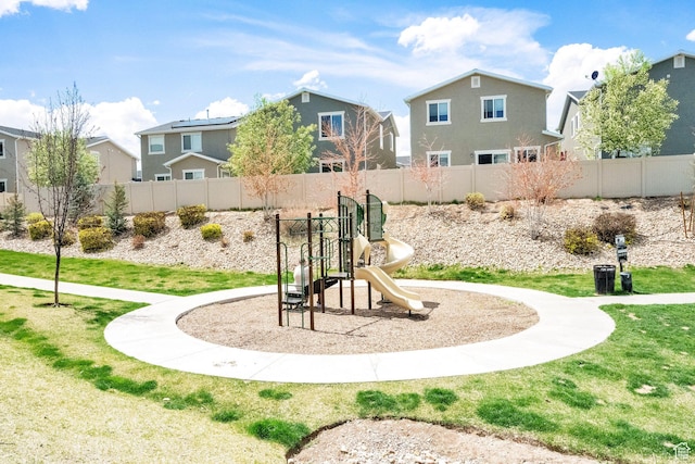 communal playground featuring fence, a lawn, and a residential view