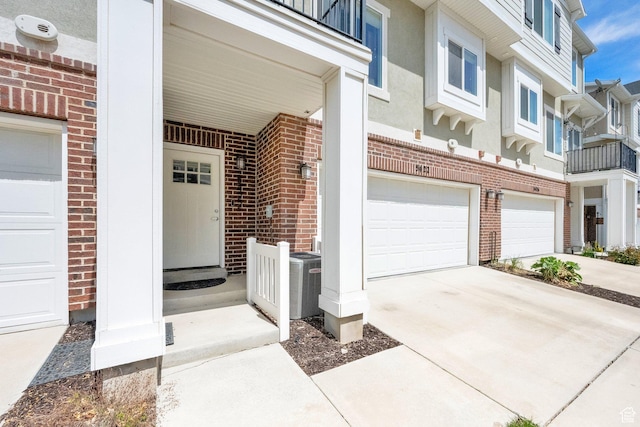 entrance to property featuring central air condition unit, brick siding, concrete driveway, and a garage