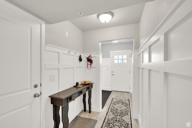 doorway to outside featuring a wainscoted wall, a decorative wall, and light wood finished floors