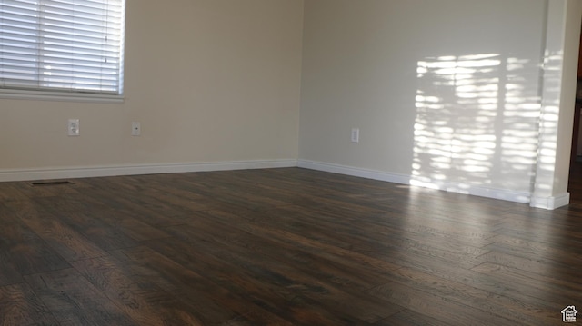 empty room with dark wood-style flooring, baseboards, and visible vents