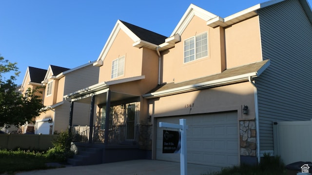 back of property with fence, an attached garage, stone siding, stucco siding, and covered porch