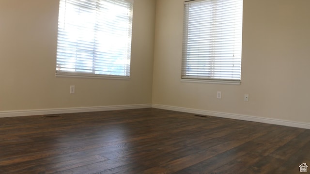 spare room featuring baseboards, dark wood-style flooring, and visible vents
