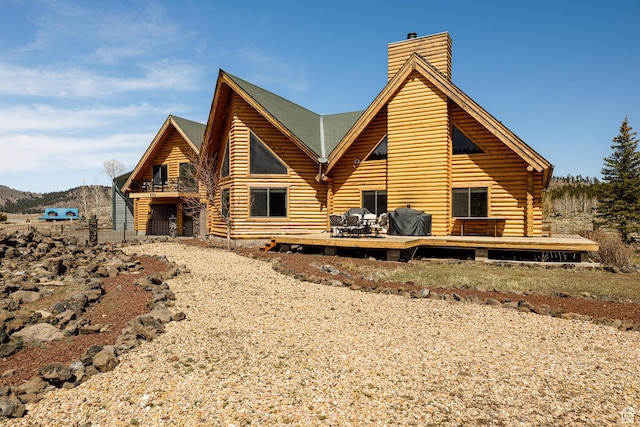 rear view of house with a wooden deck, log exterior, and a chimney