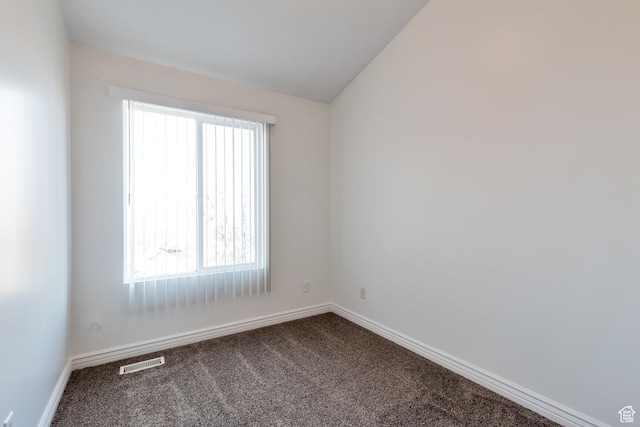 unfurnished room featuring baseboards, vaulted ceiling, dark carpet, and visible vents