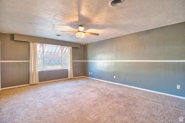 carpeted spare room featuring visible vents, a textured ceiling, ceiling fan, and wainscoting
