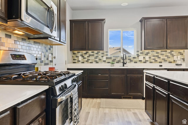 kitchen featuring dark brown cabinetry, appliances with stainless steel finishes, a sink, light countertops, and light wood finished floors