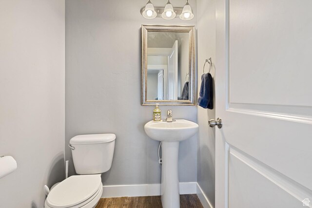 half bathroom featuring baseboards, a sink, wood finished floors, and toilet
