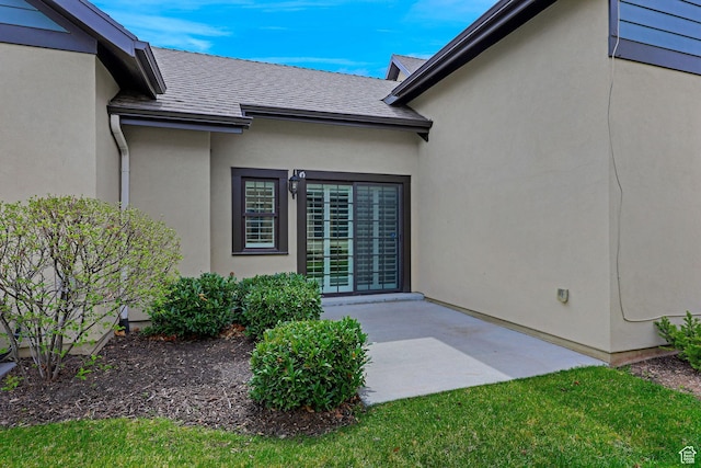 doorway to property featuring a shingled roof, a patio area, and stucco siding