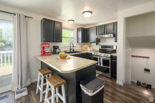kitchen with a sink, a breakfast bar area, a peninsula, double oven range, and under cabinet range hood