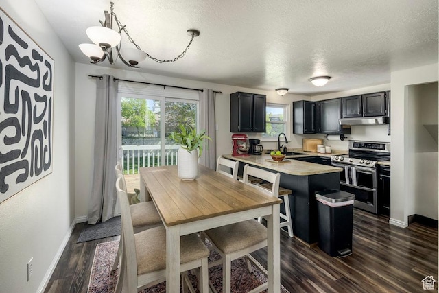 kitchen with double oven range, light countertops, a peninsula, dark cabinetry, and under cabinet range hood