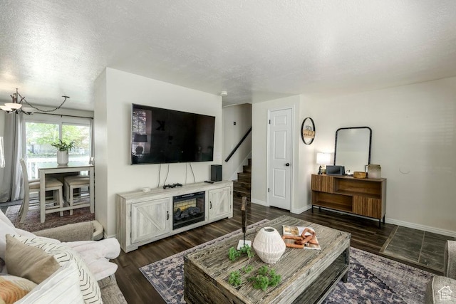 living room featuring a textured ceiling, stairway, baseboards, a chandelier, and dark wood-type flooring