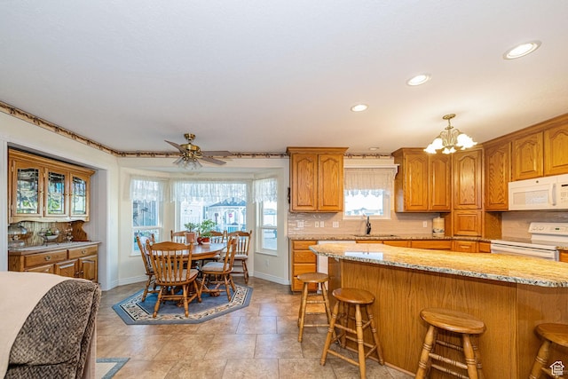 2983 W 2600 N, Plain City, UT 84404 - kitchen with backsplash, a kitchen bar, white appliances, and brown cabinetry