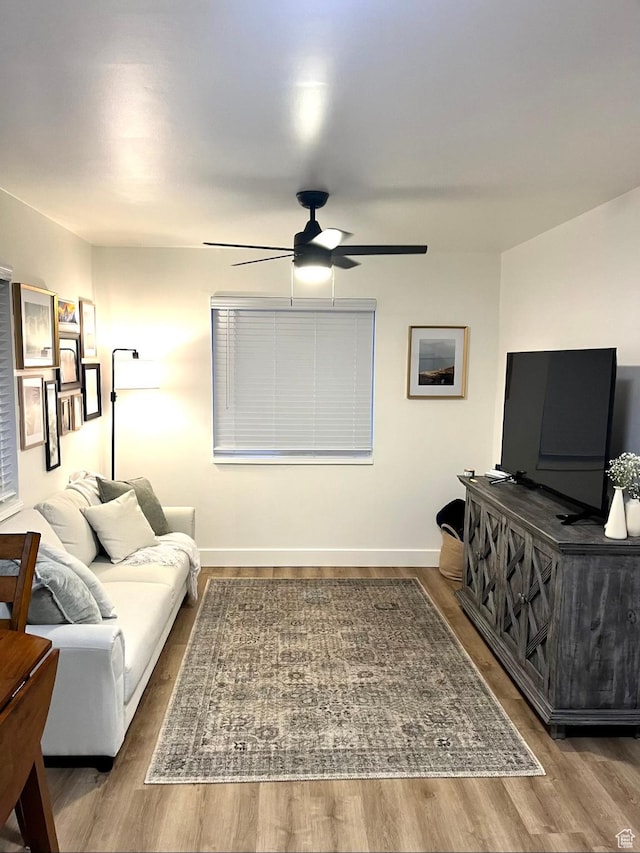 living area featuring baseboards, a ceiling fan, and wood finished floors