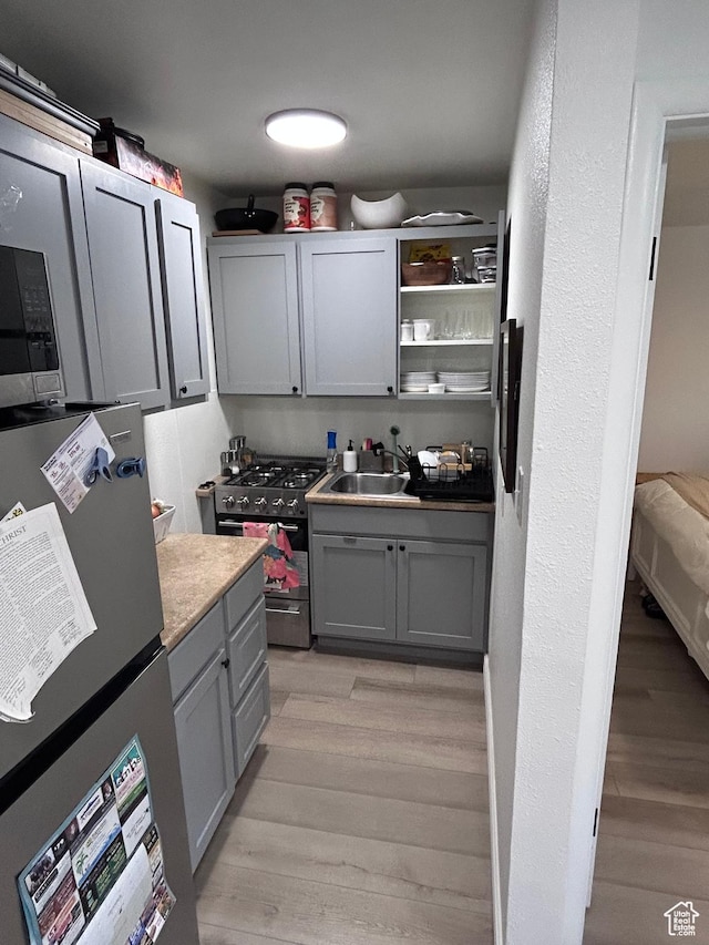 kitchen featuring stainless steel appliances, gray cabinetry, a sink, and light wood finished floors