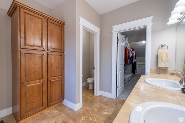 full bath with toilet, double vanity, and a walk in closet
