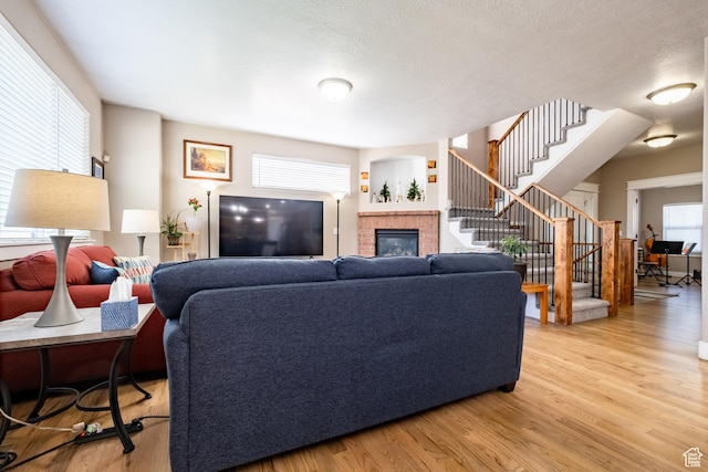 living area featuring a brick fireplace, stairs, and light wood-style flooring