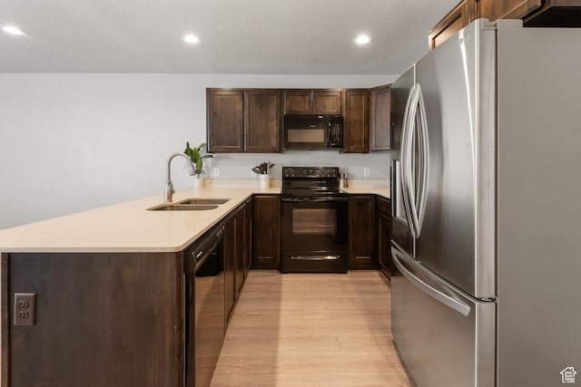 kitchen with dark brown cabinetry, a sink, light countertops, black appliances, and light wood finished floors