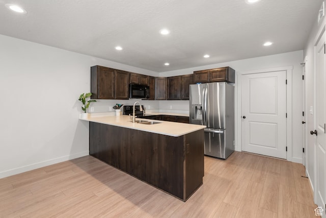 kitchen featuring dark brown cabinetry, black microwave, stainless steel fridge, light countertops, and a peninsula